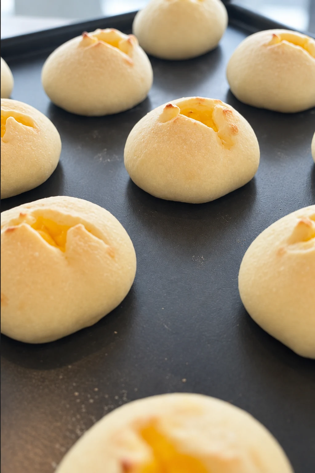 黒い天板に並ぶ、黄色いクリームがのぞく白い丸パン